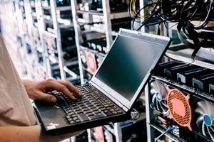 Person arbeitet mit einem Laptop vor einer Hardware-Infrastruktur