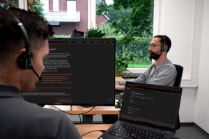Zwei Mitarbeiter mit Headsets arbeiten an Computern in einem Büro