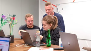 Drei Personen schauen auf einen Laptop